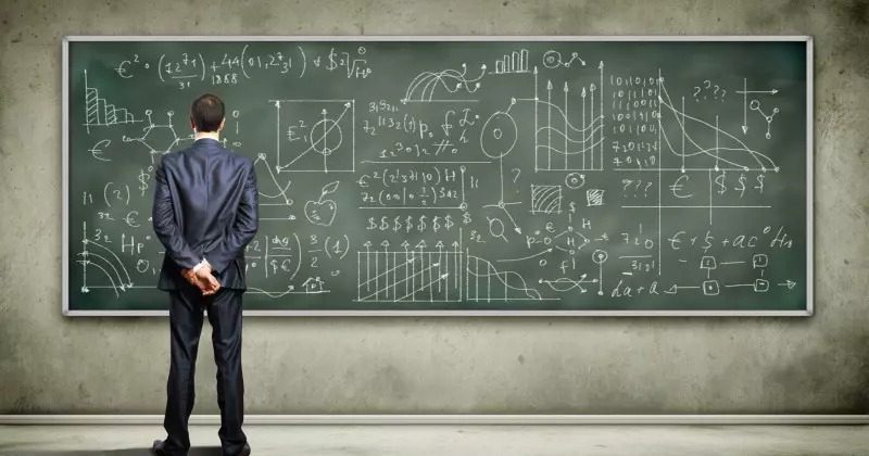 A man in a suit stands with his hands behind his back, looking at a large chalkboard filled with complex mathematical equations, charts, and graphs—meticulously analyzing the data to ensure account alignment throughout the organization.