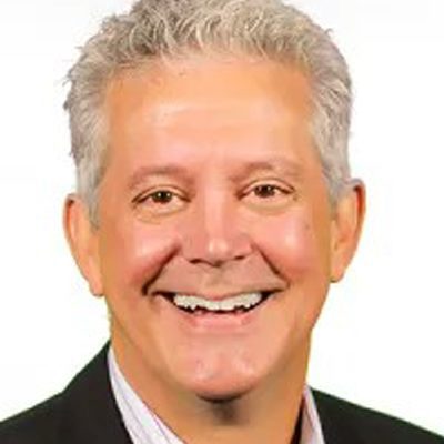 A middle-aged man with short gray hair smiles at the camera, wearing a dark suit jacket and a light-colored collared shirt, against a plain white background—perfectly embodying the professionalism often highlighted in Case Stories.